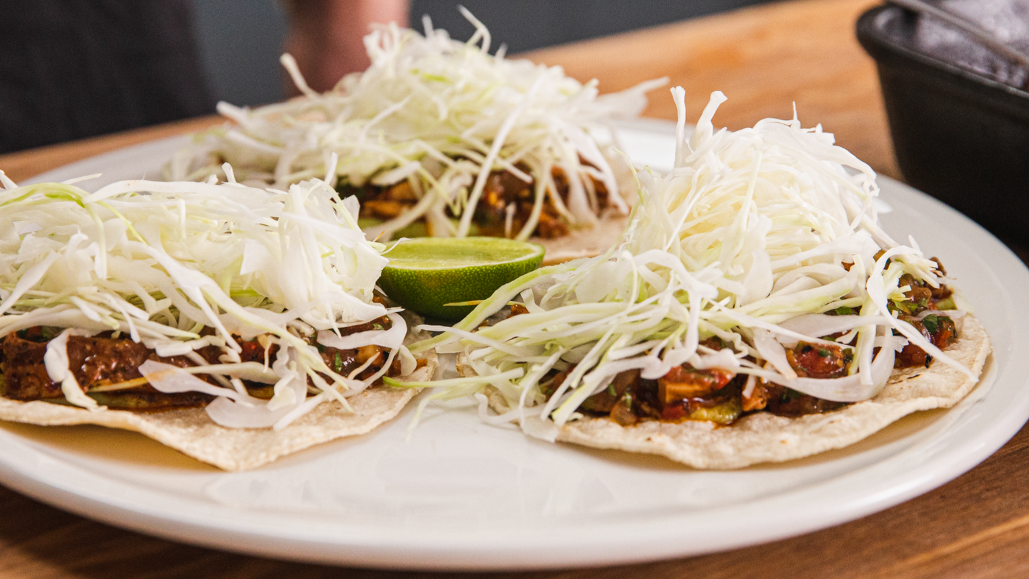 Three chicken tacos arranged on a plate with half a lime in the middle.